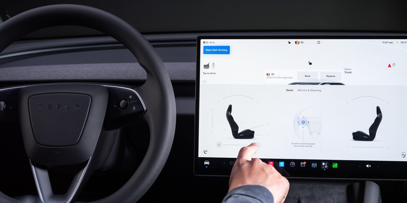 Tesla Model 3'te merkezi dokunmatik ekrandan koltuk ayarlarını yapan el ve direksiyon